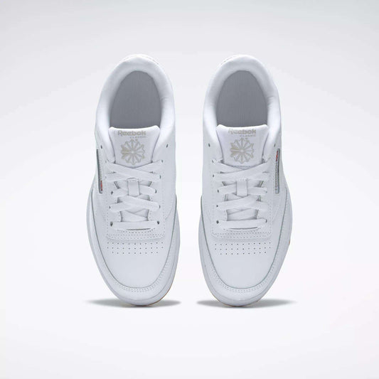 A pair of Kids' Club C Shoes - Grade School by Reebok, seen from above, with clean white leather uppers, laces, perforated toes, and Reebok logos on the tongues. The classic court style is displayed side by side on a light background.