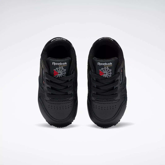 A pair of Reebok Kids' Classic Leather Shoes for baby & toddler in black, viewed from above with the Reebok logo and a red and white emblem on the tongues, set against a plain white background—ideal for young fans of classic sneakers.