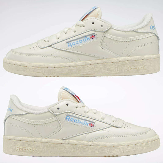 Two off-white Reebok Women's Club C 85 Vintage Shoes with cream soles are shown side by side. They feature light blue Reebok logos and a small Union Jack flag on the leather upper, set against a plain white background.