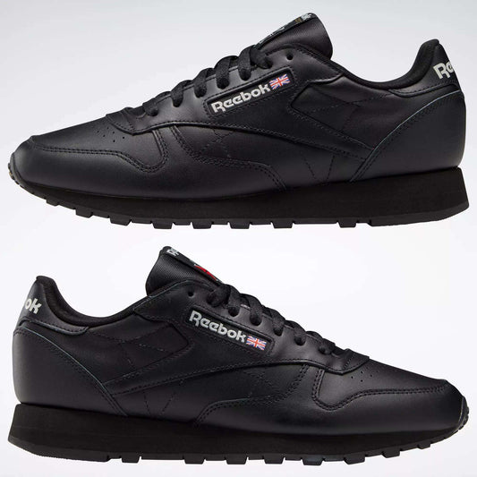 Two Reebok Classic Leather Shoes in black are displayed side by side on a white background, featuring the Reebok logo and British flag near the laces, minimalist stitching, and black rubber soles.