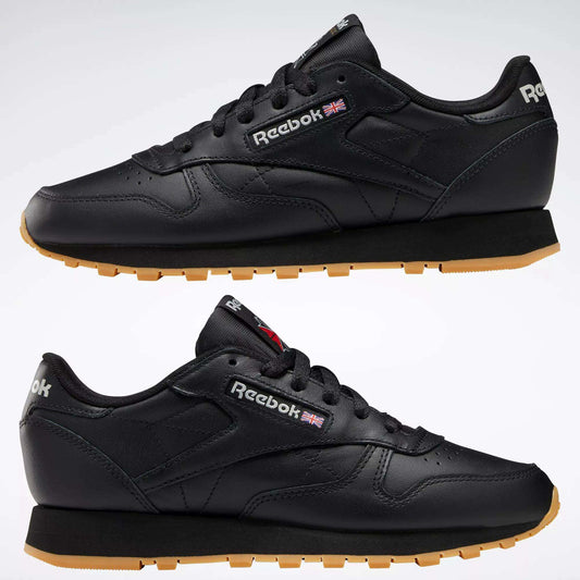 A side view of Reebok Women's Classic Leather Shoes in black with gum soles; visible features include cushioned midsoles, Reebok logos, and a small UK flag on the side and heel.