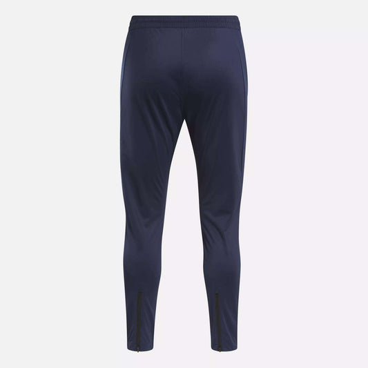 The Reebok Men's Workout Ready Track Pant in navy blue features a slim fit, elastic waistband, and ankle zippers—ideal as workout pants for any training session. Shown from the back.