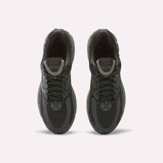 A pair of Reebok Premier Trinity women’s shoes in dark gray, viewed from above, with mesh uppers, laces, and logo patches on the tongues, side by side on a white background—ideal for running.