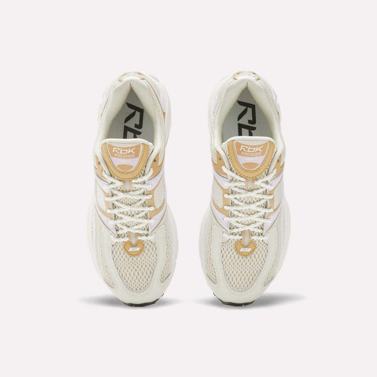 Top view of Women's Premier Trinity Shoes by Reebok in cream and beige, featuring white laces, mesh uppers, and branded tongues, inspired by retro tech running shoes, displayed on a white background.