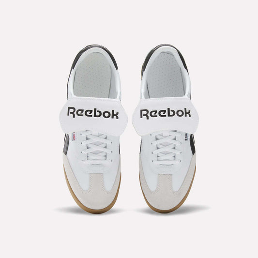 The Reebok Campio XT Kilty Shoes feature a tennis-inspired style with white uppers, beige suede toe caps, brown gum soles, black accents, and large white velcro straps with the bold black Reebok logo.