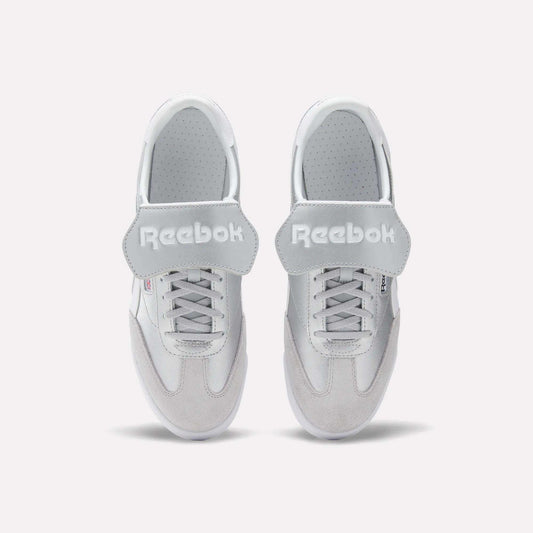 A pair of Reebok Campio XT Kilty Shoes in white leather are shown from above, side by side on a plain white background. They feature laces, wide velcro straps across the top, and the Reebok logo in white text.