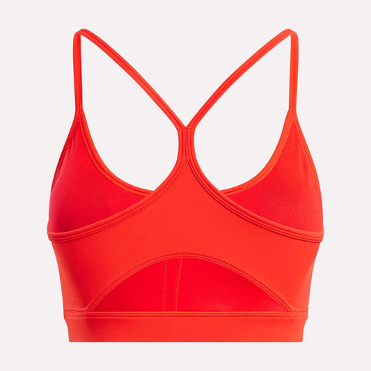 The Reebok Women's Core Strappy Bra - Medium Support in bright red features thin crisscross racerback straps, dries quickly, and is ideal for medium-impact workouts. Shown from the back on a plain white background.