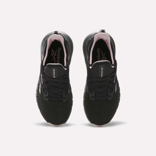 A pair of Reebok Women's Nano Gym Training Shoes in black with white soles and pink accents, shown from above on a white background. Versatile for workouts, they feature the Reebok logo on the insoles.