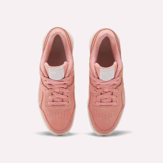 A pair of Women's Workout Plus Shoes by Reebok in pink with white soles, top view highlighting laces, perforated toes, and a white logo patch on the tongue—ideal for capturing vintage 80s workout style.
