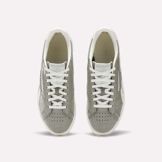A pair of Reebok Women's Club C Grounds UK shoes in grey with white laces and soles, shown from above on a plain white background. These court-inspired shoes have perforated toes and a clean white inner lining.