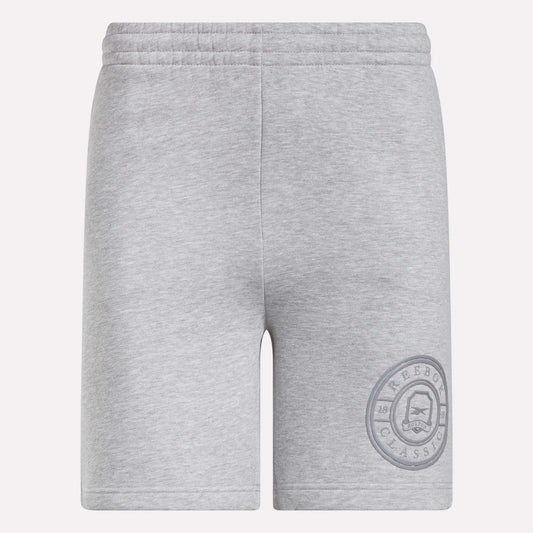 Reebok Men's Crest Shorts in light grey feature an elastic waistband and relaxed fit. Made from cotton, these shorts have a simple design without visible pockets or drawstrings and display a circular Reebok Classic logo on the lower left leg.