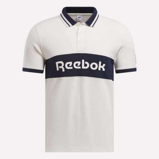 The Men’s Lawn Club Polo Shirt by Reebok is crafted in a soft cotton blend, featuring navy stripes on the collar and sleeves and a bold navy chest band with a white Reebok logo.