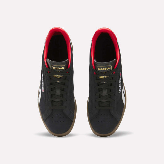 A pair of Reebok Club C Grounds UK Shoes in black with white side stripes, gold and red accents, black laces, and gum soles are shown from above on a white background—a perfect classic tennis-style casual shoe.