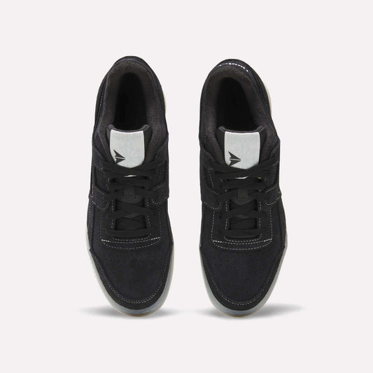 A pair of Reebok Workout Plus Shoes in black with white stitching and tongue labels, seen from above on a light background. The tied laces and side-by-side placement highlight their classic '80s-inspired fitness style.