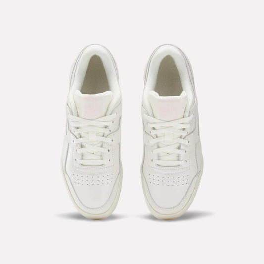 The Reebok Women's Workout Plus Shoes in white are shown from above, highlighting laces, stitching, and perforated toe boxes for classic '80s fitness style against a plain light background.