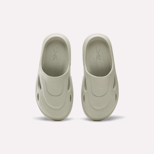 The Reebok DMX Recovery Mules in light beige are shown on a plain white background, featuring molded EVA design, rounded toes, side ventilation holes, and textured insoles inspired by DMX Moving Air tech.