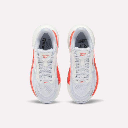 Top view of Women's FloatZig Double Running Shoes by Reebok, in white with bright orange side accents and branded tongue, set against a plain light background.