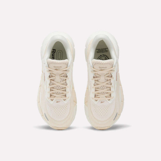 A pair of Women's FloatZig Double Running Shoes by Reebok in beige are shown from above, featuring laces, mesh texture, and logo details on the tongues—designed for max-cushioned runs—set against a plain white background.