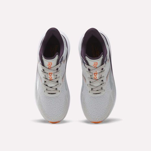 Top view of a pair of Reebok Women's Viva Speed Shoes in light gray with purple accents, featuring an orange logo on the tongue, white laces, and lightly patterned mesh uppers, placed side by side on a plain white background. These breathable running shoes offer a cushioned midsole for enhanced comfort with every stride.