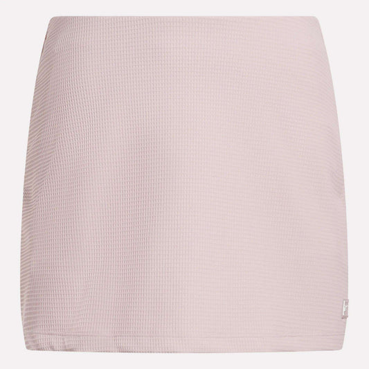 The Reebok Women's Time Out Slim Tennis Skort features a light pink, waffle-textured fabric and straight cut—a minimal design ideal for sporty flair in your activewear wardrobe. Shown against a white background.