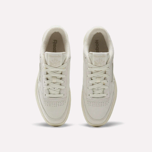 Top view of men's Reebok Club C Revenge Shoes in cream, featuring white laces, perforated nubuck leather toes, and visible Reebok logos on the tongues, set on a plain white background.