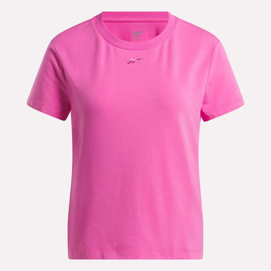 The Women's Graphic Glow Top by Reebok is a pink, short-sleeved shirt with a round neckline and a subtle embroidered logo on the chest, shown against a white background.