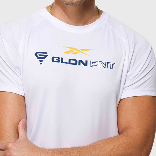 A man wears a Reebok x GLDN PNT Tech Tee featuring a yellow and blue logo on the chest. Only his upper torso and arms are shown, with his face not visible. The lightweight tee is crafted from Reebok’s moisture-wicking fabric.