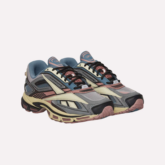 Reebok Premier Road Ultra Shoes feature mesh uppers, chunky dual-density midsoles, and lace-up closures in gray, cream, navy blue, and pink accents, shown against a light blue background.
