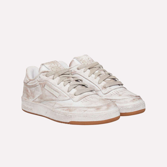 A pair of beige Reebok Club C 85 Vintage sneakers with tied laces, a slightly distressed finish, and gum soles—an iconic classic—are positioned side by side on a white background.