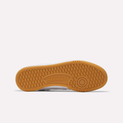 The Women's Club C 85 Shoes by Reebok feature a gum-colored rubber sole with herringbone tread and a circular toe design embossed with the Reebok logo, shown from the bottom—perfect for women.