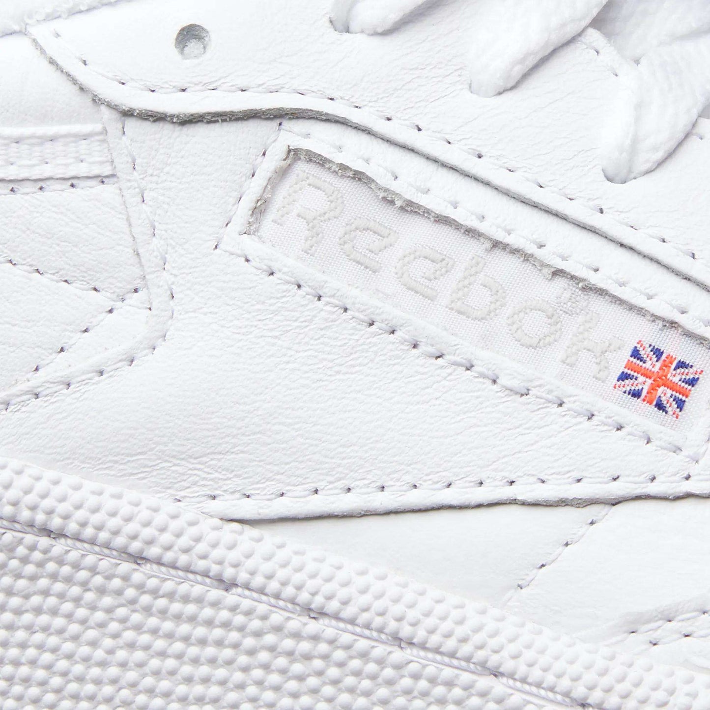 Close-up of the Reebok Women's Club C 85 Shoes highlights the logo, a small UK flag patch, and detailed leather stitching—making these sneakers a timeless choice.