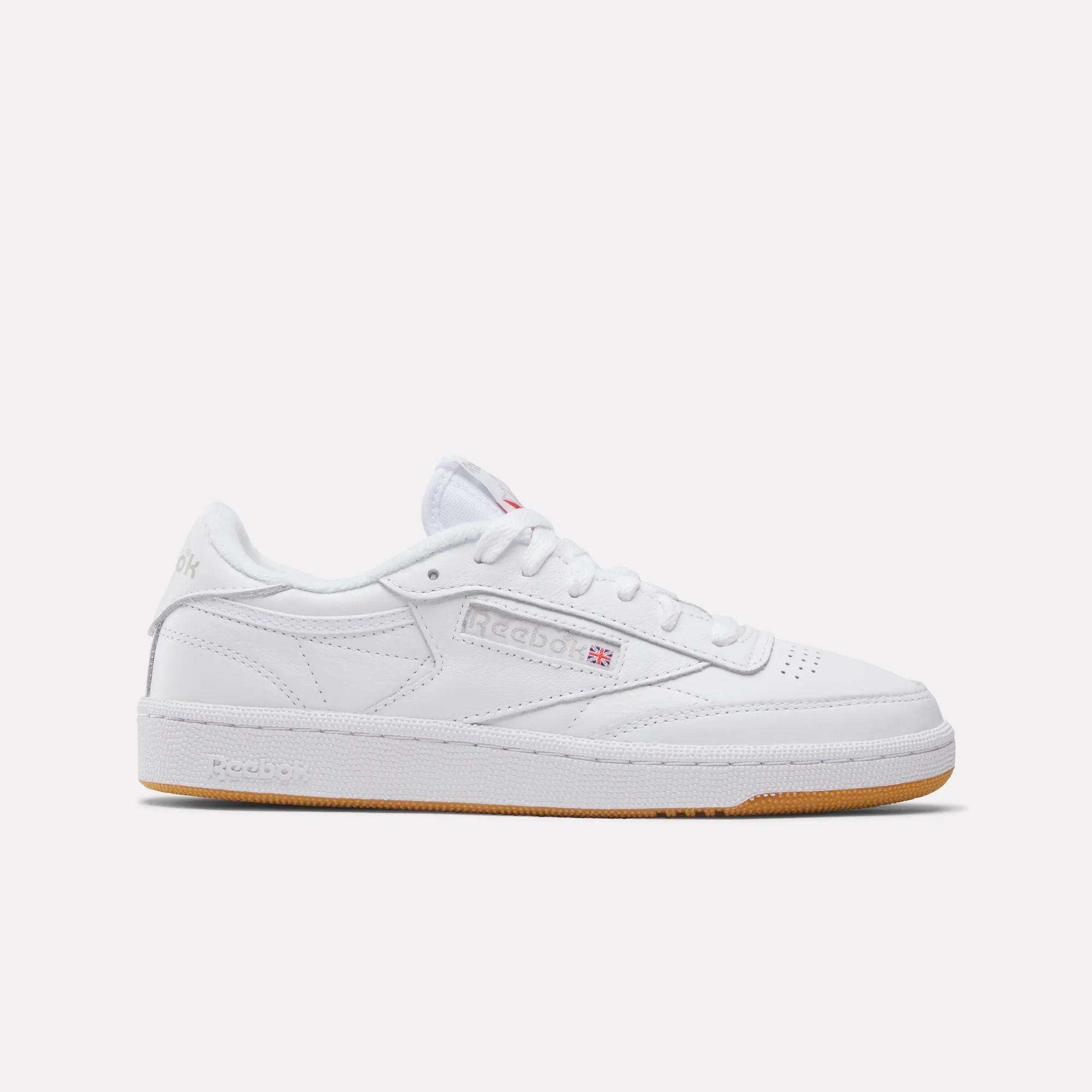 The Reebok Women's Club C 85 Shoes feature a white low-cut design, perforated toe, white laces, subtle branding, and a light brown rubber sole; shown on a plain white background.