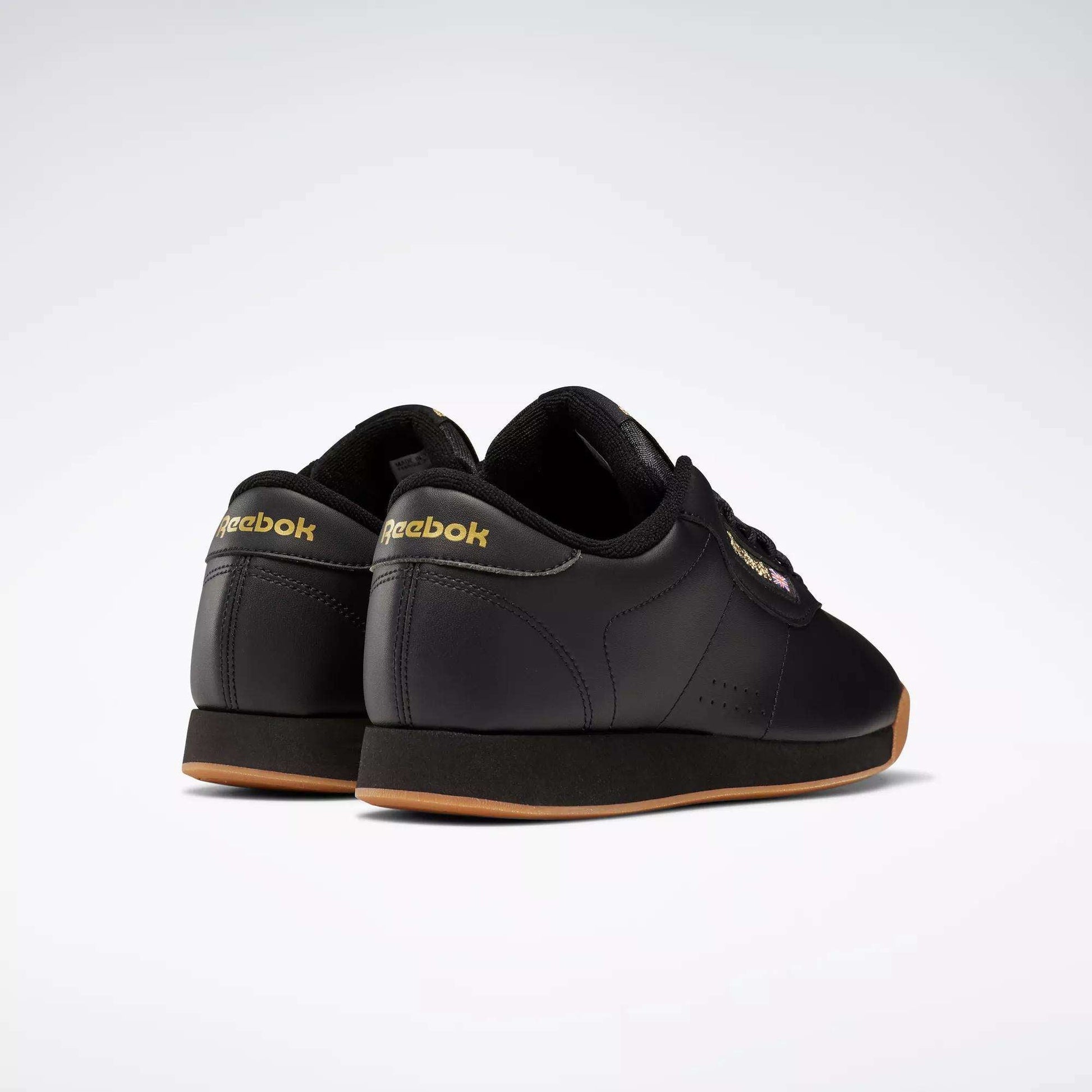 Women's Princess Shoes by Reebok in black feature gum soles and heritage-style gold Reebok logos on the heel and sides. Shown from the back and side against a plain white background.