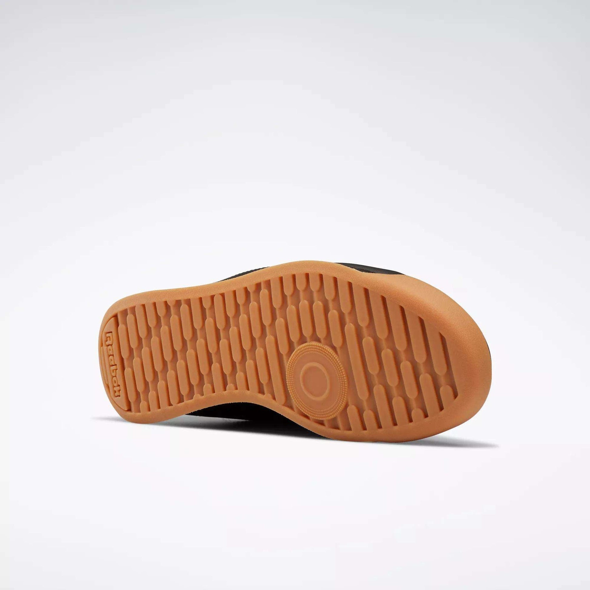The image shows the sole of Reebok Women's Princess Shoes against a light gray background. The light brown sole features a textured, grippy pattern with a circular design near the ball of the foot and the Reebok logo by the heel.