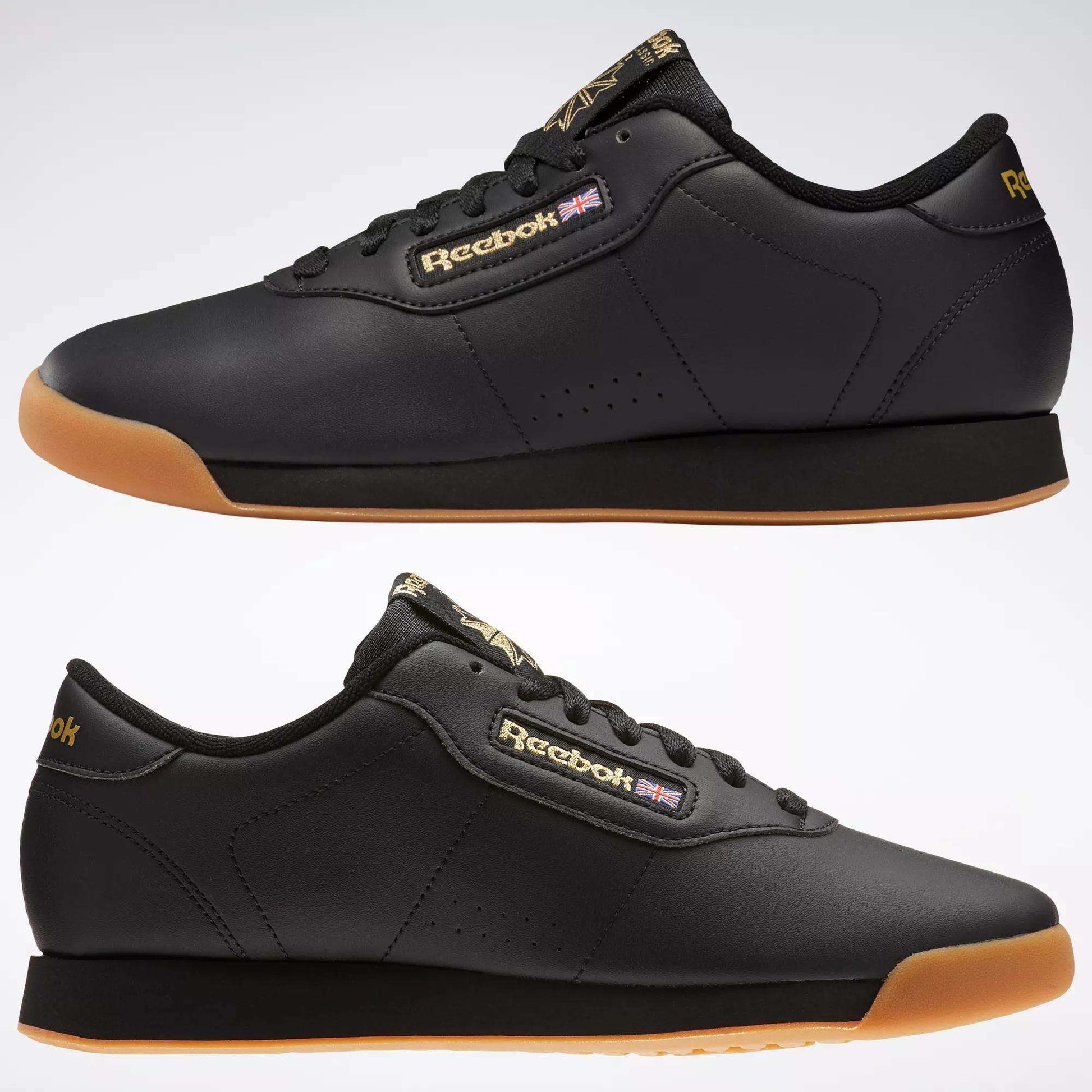 Two black Reebok Women's Princess Shoes with gum soles are shown from the side on a light background. Featuring the Reebok logo and Union Jack, these sneakers blend heritage style with modern comfort.