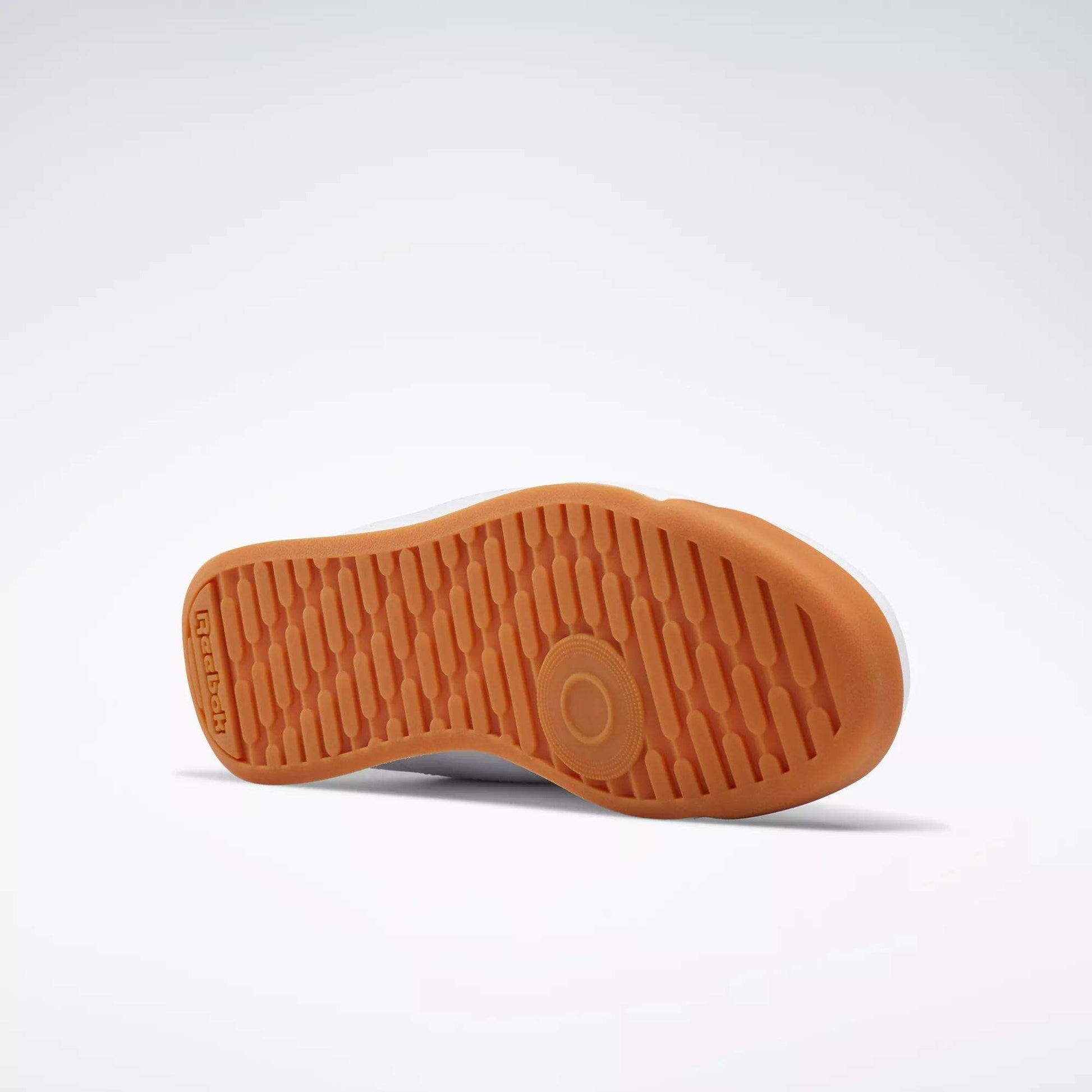 A Reebok Women's Princess Shoe rests on its side, displaying the textured orange rubber sole with Reebok branding and a circular grip pattern for extra cushion against a plain light background.