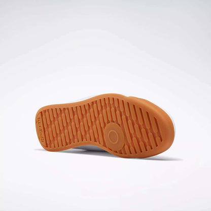 A Reebok Women's Princess Shoe rests on its side, displaying the textured orange rubber sole with Reebok branding and a circular grip pattern for extra cushion against a plain light background.