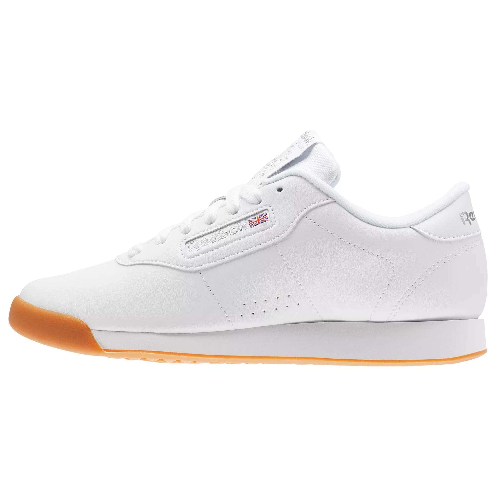 The Women’s Princess Shoes by Reebok are classic white sneakers featuring a cushioned footbed, gum sole, low-top design, perforated sides, and signature Reebok branding.