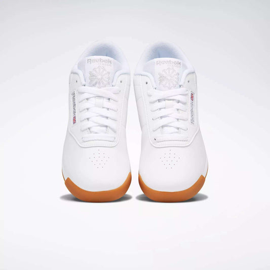 A pair of Reebok Women's Princess Shoes in white with gum soles, shown from above on a plain light background. These sneakers feature Reebok logos, toe perforations, and provide excellent cushioning for all-day comfort.