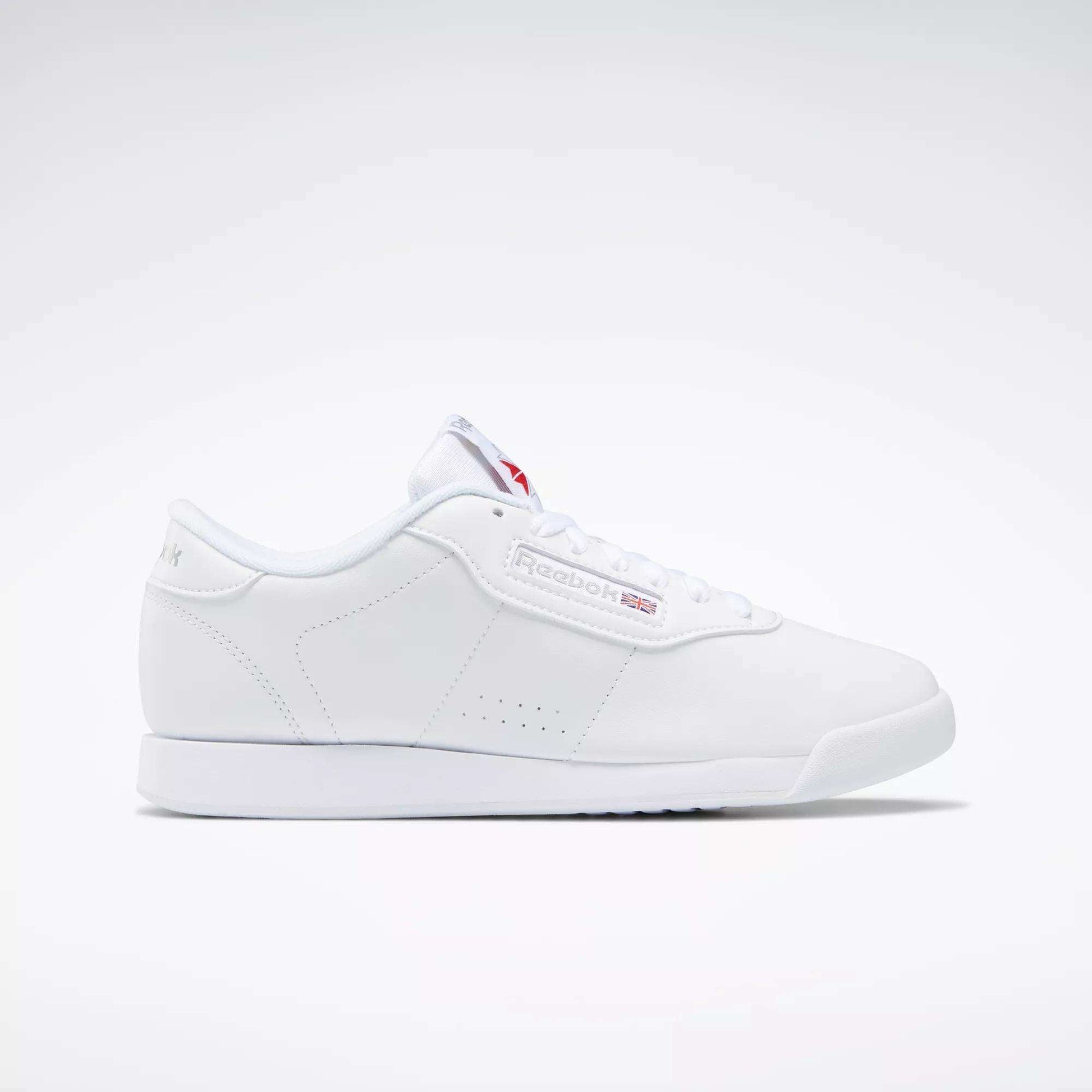 The Reebok Women's Princess Shoes feature a classic white design with a flat sole, cushioned comfort, and subtle branding on the side and tongue—a timeless choice displayed on a plain light background.