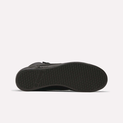 The Reebok Women's Freestyle Hi Shoes in black feature a textured rubber outsole with a hexagonal pattern and visible branding near the heel—ideal for women's fitness or as a stylish high-top option.