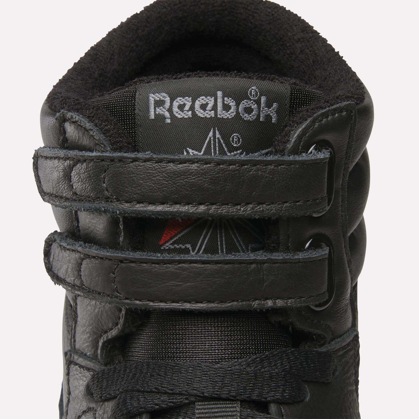 Close-up of the Women's Freestyle Hi Shoes by Reebok, showing the black high-top design with a padded collar, visible stitching, two velcro straps across the front, and the Reebok logo on the tongue.
