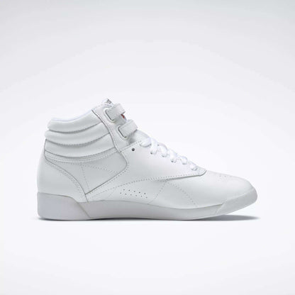 The Reebok Women's Freestyle Hi Shoes are white high-top sneakers with laces and velcro straps, showcasing a minimalist design and subtle stitching—perfect for women's fitness routines. Shown in a side view on a plain light background.