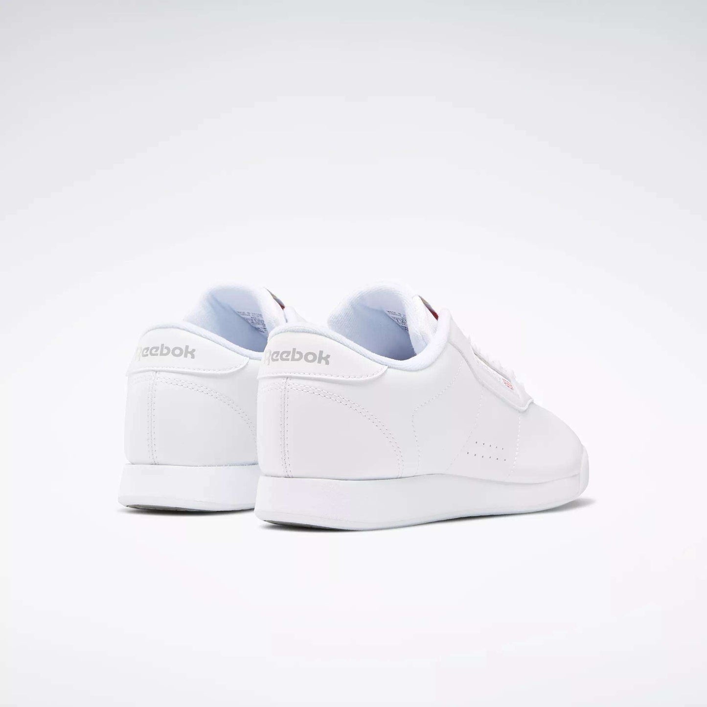 The Reebok Women's Princess Wide Shoes are shown from the back and side against a light background, featuring subtle stitching, a heritage cushion sole, and Reebok logos with Union Jack detail on the heel and side.