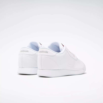 The Reebok Women's Princess Wide Shoes are shown from the back and side against a light background, featuring subtle stitching, a heritage cushion sole, and Reebok logos with Union Jack detail on the heel and side.