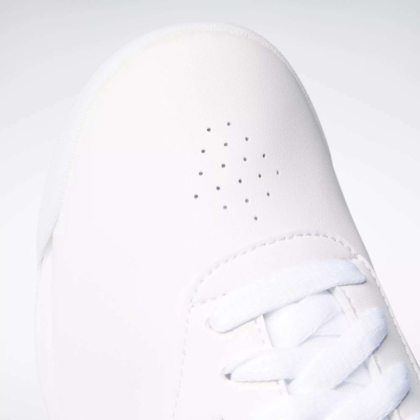 Close-up of Reebok Women's Princess Wide Shoes with small perforated holes and white laces at the toe. The plain, light background highlights the sneaker’s timeless Reebok style.