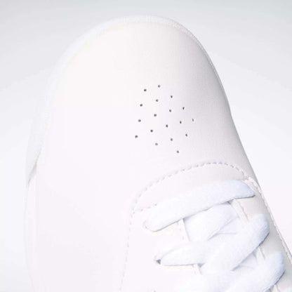 Close-up of Reebok Women's Princess Wide Shoes with small perforated holes and white laces at the toe. The plain, light background highlights the sneaker’s timeless Reebok style.