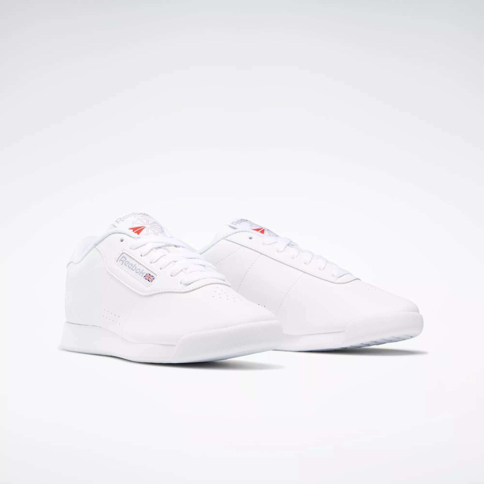 The Women's Princess Wide Shoes by Reebok feature a classic, minimalistic design with the iconic Union Jack logo and branding on the side, showcased against a plain white background.