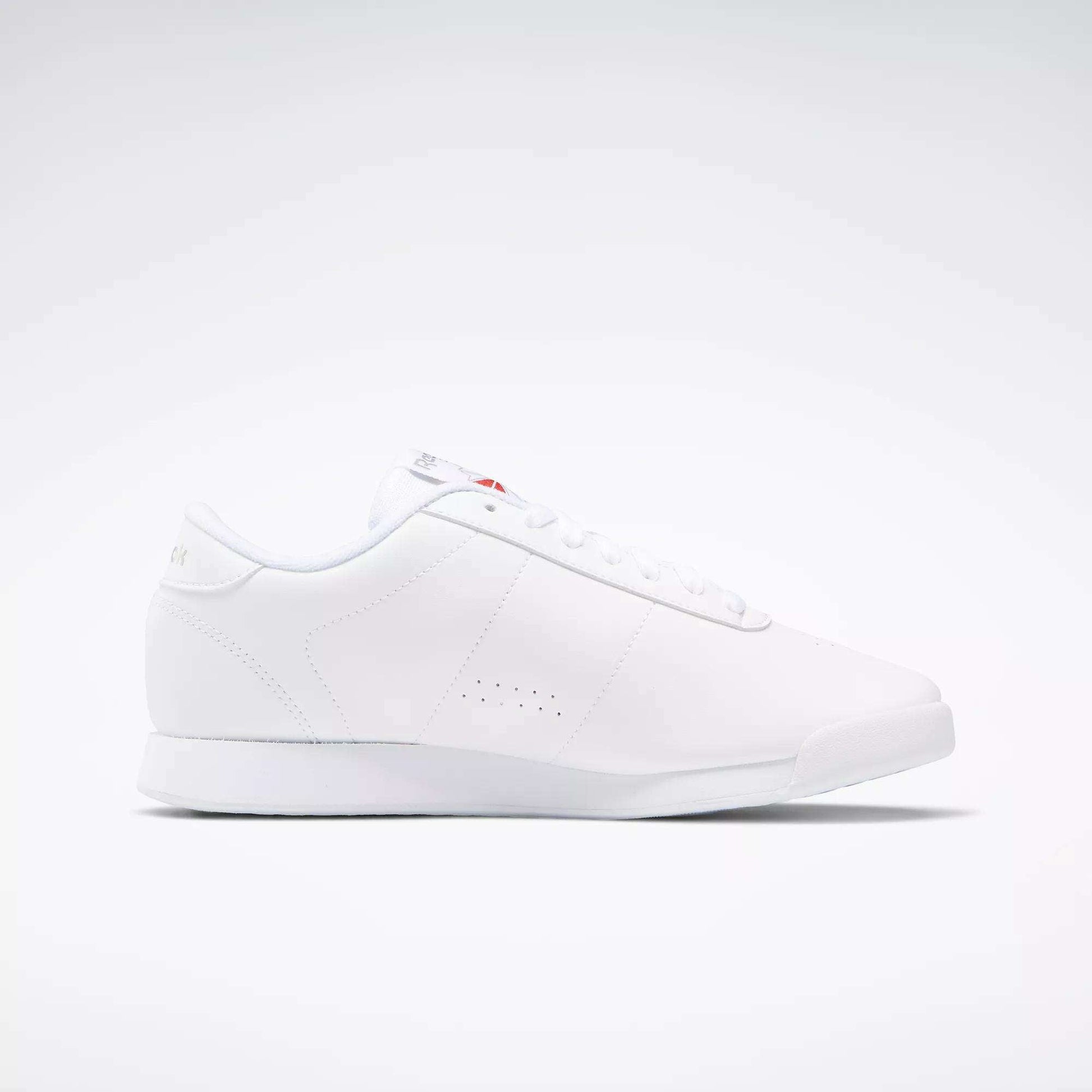 The Reebok Women's Princess Wide Shoes are white low-top sneakers with a minimalist design, flat sole, subtle side perforations, white laces, and a discreet Union Jack logo—highlighting classic women's shoe heritage—shown on a plain white background.