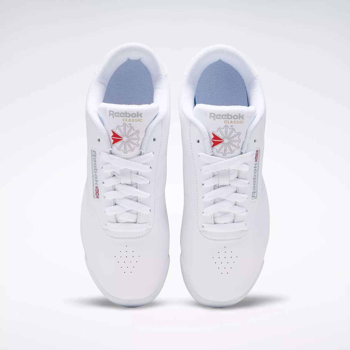 A pair of classic Reebok Women's Princess Wide Shoes with white laces, viewed from above. These sneakers display the Union Jack logo in red and gray on the tongue and side, set against a plain white background.